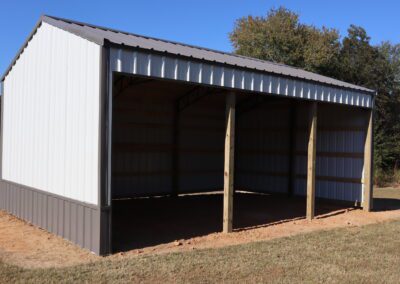 Open-sided metal shed on a grass field with a clear sky in the background.
