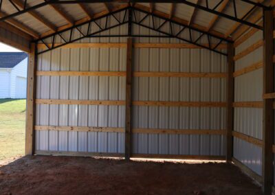 Interior of an empty metal barn with wooden framing and dirt floor.