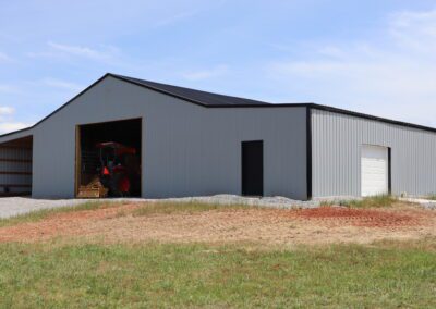 A large metal barn with an open door showing a tractor inside, under a clear blue sky.