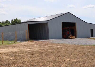 A large metal barn with an open door showing a tractor inside, under a clear blue sky.