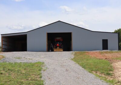 A large metal barn with an open door showing a tractor inside, under a clear blue sky.