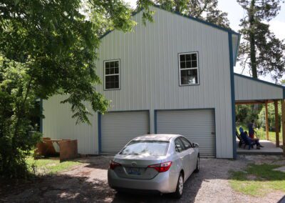 A metal-clad house with a front porch where two people sit, surrounded by lush greenery.