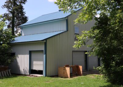 A metal-clad house with a front porch where two people sit, surrounded by lush greenery.