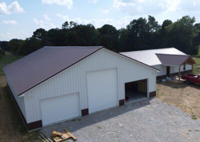 Aerial view of a large white barn with red trim and a red truck parked outside.
