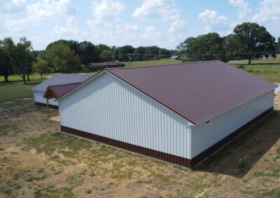 Aerial view of a large metal barn with reddish-brown roof in a grassy field.